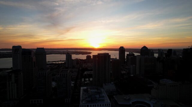 Drone flying backward at sunset with camera tilting down revealing buildings below in downtown San Diego.