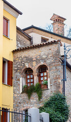 Fototapeta premium Stone building with arched windows and flower boxes, featuring a chimney, surrounded by colorful houses in Arqua Petrarca Italia