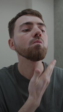 White man massaging balm into beard after trimming, gentle downward strokes, skin soothing ritual, satisfied small smile and clean