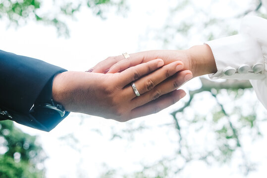 Close up of couple holding hands with silver wedding ring and smartwatch on blurred nature background.