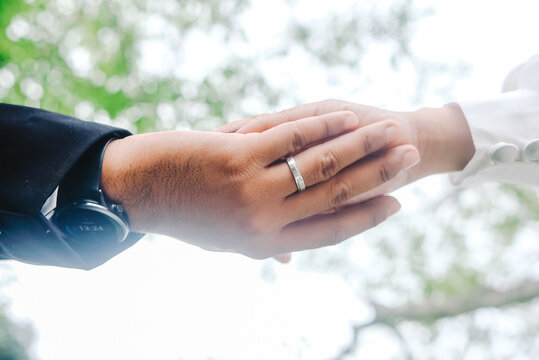 Close up of couple holding hands with silver wedding ring and smartwatch on blurred nature background.