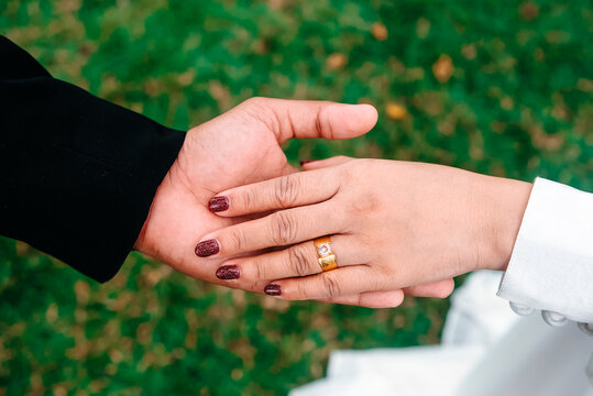Close up of a couple holding hands showing gold engagement ring on grass background.