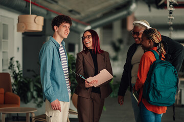 Diverse students talking with a smiling female teacher and older mentor, discussing academic support in a modern university setting