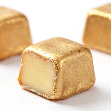 Golden-wrapped caramel candy with smooth, shiny surface. One piece cut open shows creamy white center. Soft focus on background candies. Perfect for sweet treats, luxury dessert, or holiday marketing