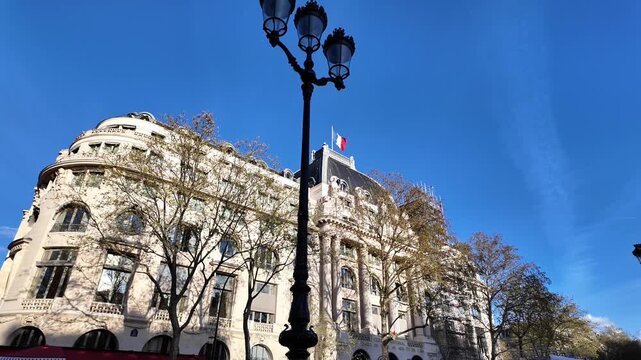 Wide static shot of the Cercle de l'Union Interalli&eacute;e historic building and the French flag waving against a clear blue sky.