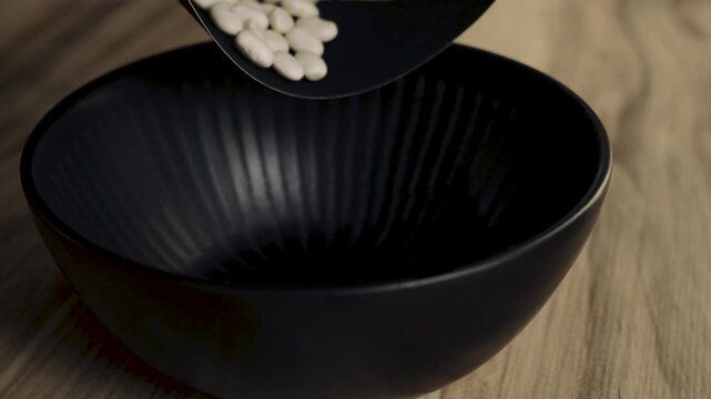 White_kidney_beans_filling_black_bowl_on_wooden_table_4k_10bit_120fps