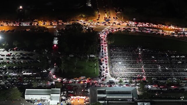 Aerial night view of vehicle light trails and parked cars at a congested intersection and parking lot at Batu Kawan Stadium
