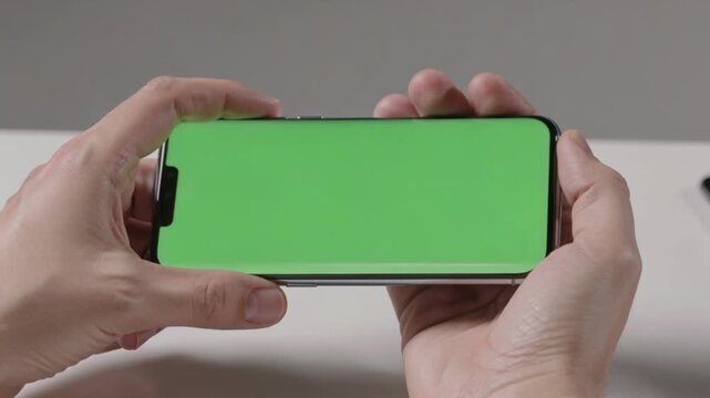 Hands holding smartphone with green screen in landscape mode for creative use