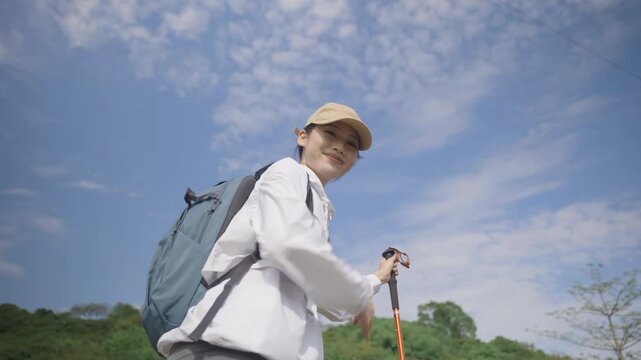 Young female hiker backpacker smiling happily, cheerfully greeting guide, waving hand, welcoming or saying goodbye, woman with backpack trekking cloth poles walk along mountain trail climb forest path
