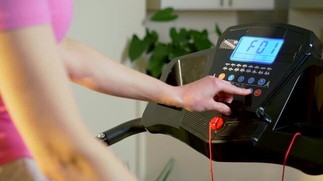 Preparing treadmill workout program on digital console before starting home cardio training. Female athlete selecting running mode and speed settings on indoor fitness machine panel. Healthy lifestyle