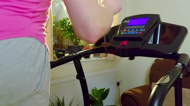 Unrecognizable runner exercising on treadmill slow motion during indoor cardio workout at home. Woman maintains steady jogging pace on compact fitness machine in bright apartment interior. Active