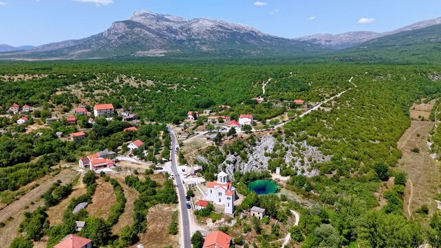 Aerial view of the Cetina River source, known as the Eye of the Earth, with the Church of the Ascension and the Dinara mountain range in Croatia