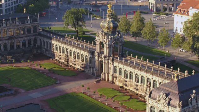 Aerial view of the Dresden Zwinger at sunset. The Crown Gate and galleries cast long shadows over the manicured courtyard with its lush green lawns and Baroque architecture.