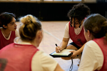Naklejka premium Coach explaining strategy to female basketball players