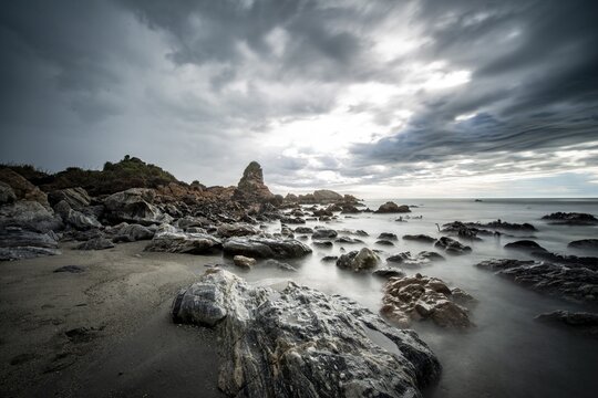 Rocky coast, rocks on the beach, dark rain clouds, long time exposure, West Coast, South Island, New Zealand