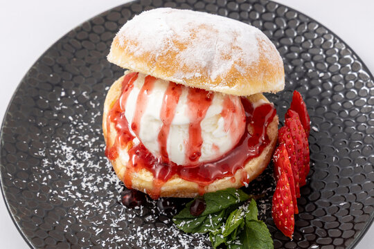 Sweet Dessert Donut with Vanilla Ice Cream, Strawberry Sauce and Fresh Strawberries on Black Plate