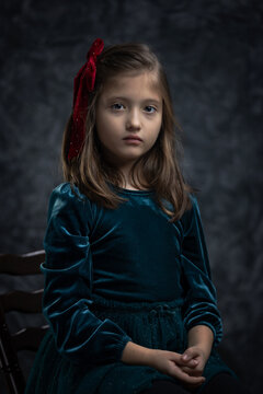 Fine art portrait of a little girl in a vintage green velvet dress. Timeless, painterly-style studio shot with a thoughtful, nostalgic mood.