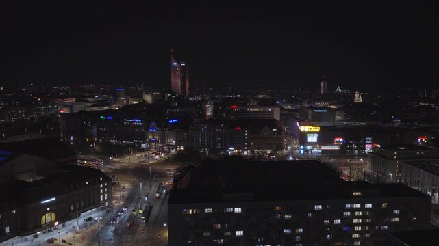 Night aerial view of Leipzig featuring the illuminated Panorama Tower. City lights and traffic create an atmospheric urban scene in the darkness.