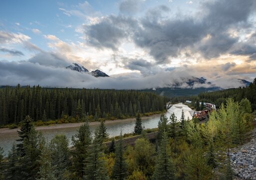 Cloudy Rocky Mountains at sunset, Morant's Curve, train farting in the curve, forested bank at Bow River, Bow Valley, Banff National Park, Alberta, Canada