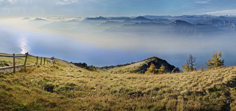 Meadow with fence and Lake Garda in the morning mist with Lake Garda mountains and Bergamo Alps, Monte Baldo, Malcesine, Verona Italy, Trentino-Alto Adige, Italy