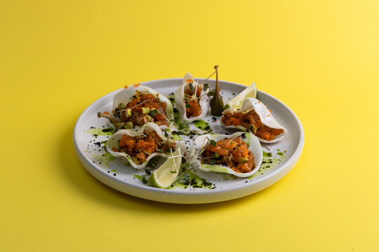 Fresh seafood tacos served on a white plate with lime and garnish on bright yellow background