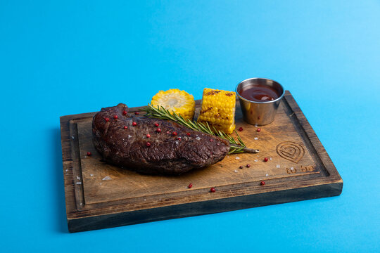 Steak served on wooden board with corn and sauce in colorful setting at restaurant during daytime