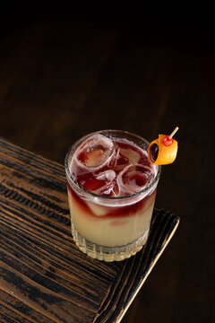 Cocktail with ice and garnish served on wooden table in a dim setting at a bar during evening hours