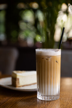 Coffee drink sits on a wooden table near a slice of cheesecake in a cozy cafe during a sunny afternoon