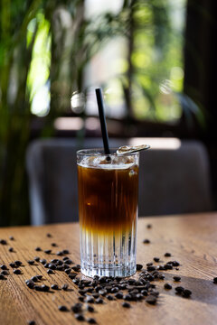 Coffee drink sits on wooden table surrounded by coffee beans in a cafe during the day with natural light coming in through windows