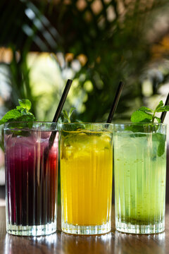 Refreshing drinks made with fruits and herbs served in clear glasses on a wooden table in a natural setting during daytime