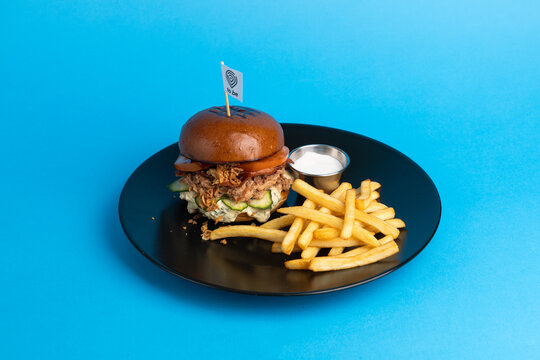 Delicious sandwich served with fries on a black plate against a blue background at a restaurant setting