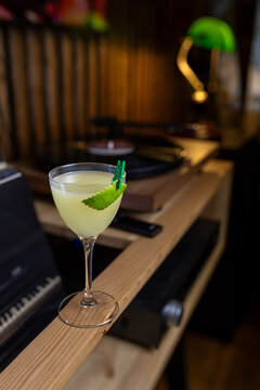 Cocktail placed on a wooden bar with turntable in the background during evening hours