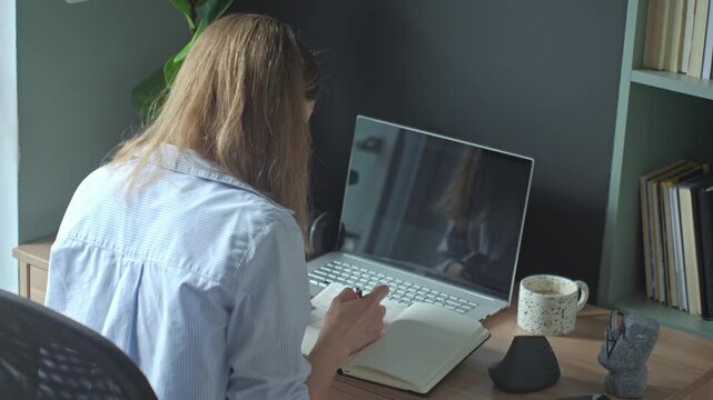 Woman drawing in sketchbook at desk with laptop, mug and mouse in home workspace. Concept of remote work and creative process