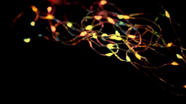 Colorful LED string lights twinkle and glow warmly against a solid black background, creating a soft bokeh effect. Concept of festive celebrations and magical holiday atmospheres.