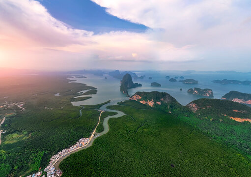 Aerial view majestic karsts rise from emerald waters around green forest jungle, fringed by winding mangroves vibrant coastal village at twilight