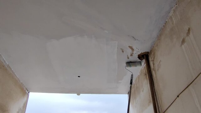 Painter rolling paint on tall ceiling with long pole roller
