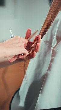 Close-up of hairdresser hands cutting long brown hair in beauty salon. Professional haircut trimming split ends of healthy female hair with scissors. Hair care, grooming and salon service concept.