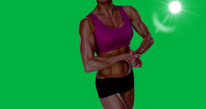 Mid section of female bodybuilder flexing her muscles against spot of light on black background