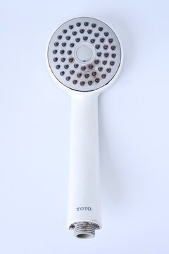 Jakarta, Indonesia - April 13th, 2026 - Old used TOTO brand white shower head isolated on vertical white background.