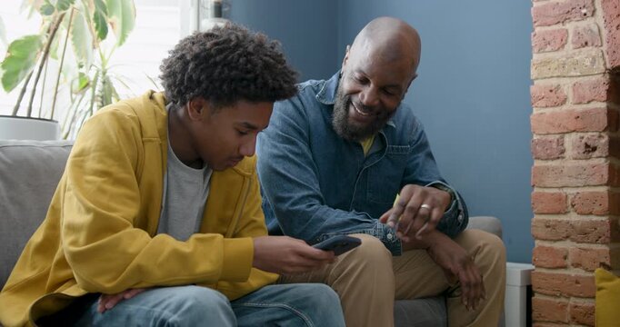 Father and Son Talking Together and Looking at Phone on Sofa at Home