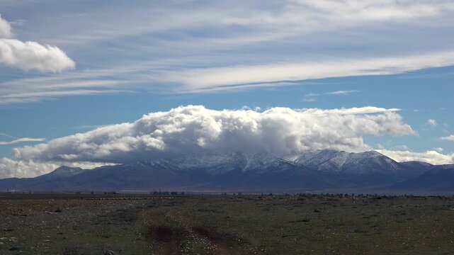 Patagonian winter mountains lie beneath dense clouds as time lapse reveals motion above cold plains. Dramatic sky and snowy peaks create an atmospheric landscape in southern Argentina.