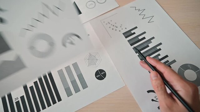A person examines printed data sheets that display various graphs and charts related to the oil market. The individual appears focused while analyzing trends and statistics on the papers