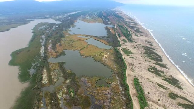 Aerial drone view of a coastal lake and wetland swamp formed by longshore drift. The current deposits sediment, creating sandpit tombolo cluster near the waterside.