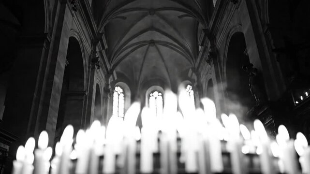 Low angle black and white shot of lit candles in an ornate cathedral interior with a high arched ceiling
