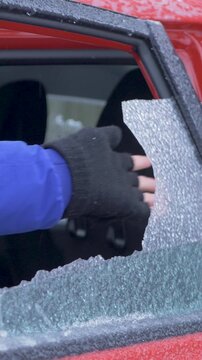 Person in blue jacket opens car door, revealing window completely covered in thick ice. Efforts to gain access to frozen vehicle emphasize harshness of winter weather and challenges it presents