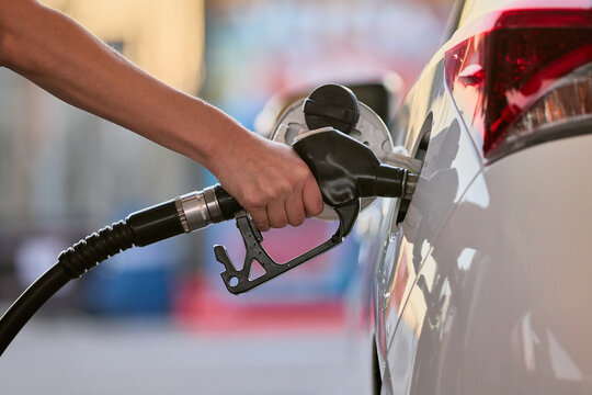 Close-up of a person refueling a car at a gas station. Fuel nozzle inserted into vehicle tank during refueling process.