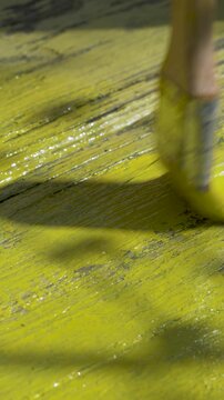 Female painter starts porch renewal. Yellow paint flows from brush to rough wood. Board changes tone quickly. Atmosphere filled with focus and care. Natural materials reflect effort