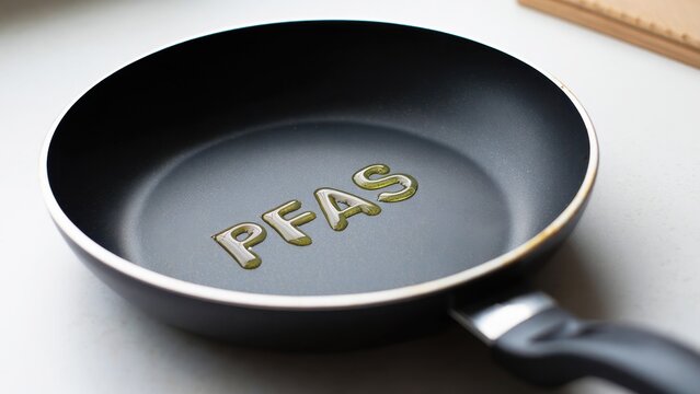 Black non-stick frying pan, PFAS liquid text inside, kitchen countertop environment, chemical safety and health research style