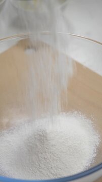 Female cook sifts wheat flour through metal sieve. White powder falls into transparent bowl. Starts process of dough preparation in home kitchen