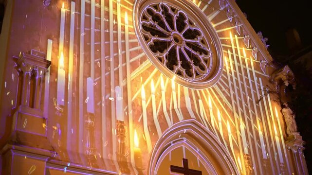 Illuminated church facade with projection mapping of candles and festive lights at night.